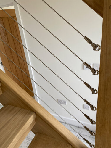 Detail of a premium stainless steel wire system installed in a wooden stair railing at Beach House in East Sussex.