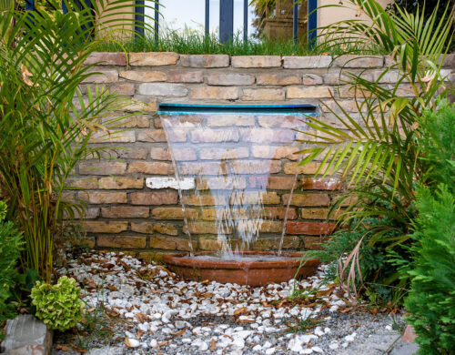 Wide water blade mounted in brick wall in garden in Kent