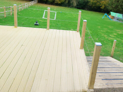 Wooden decking with posts and wire rope balustrade installed in a garden in Chertsey by River.ODP installation company.