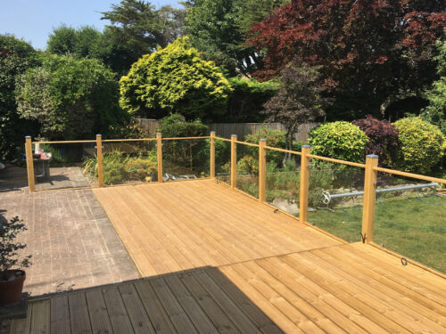 Wood and glass balustrade mounted on large timber decking in Pevensey by installation company River.ODP