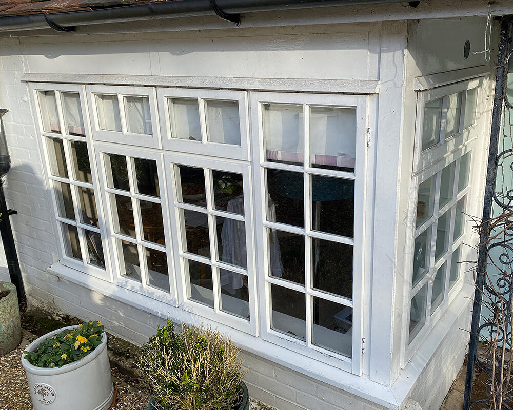 OLD broken white wooden bay window with bars mounted in house in Hailsham.