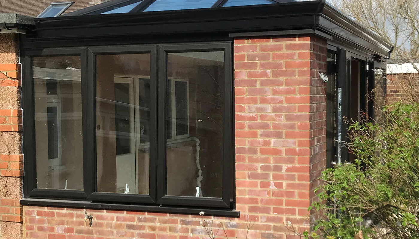 Bespoke build orangery extension in Eastbourne garden with black windows, French doors and lantern on the roof. Side view from the pond