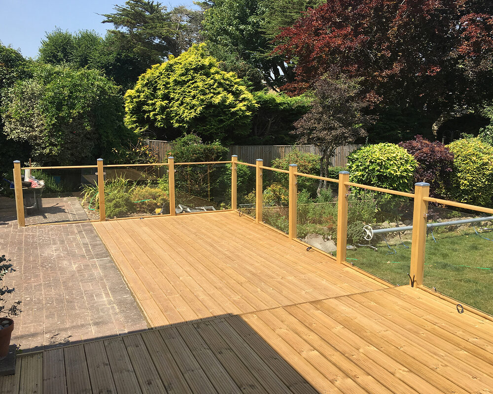 Wood and glass balustrade mounted on large timber decking in Pevensey by installation company River.ODP