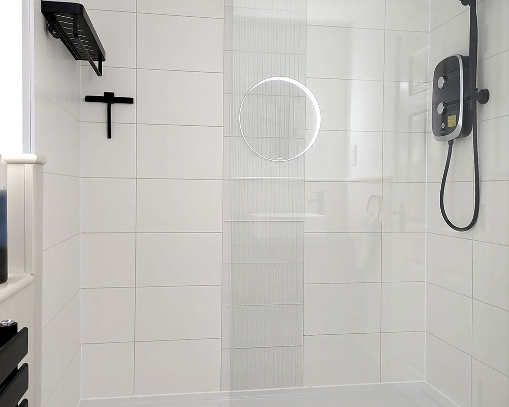 A modern shower enclosure with white tiled walls, a glass screen and matching black fixtures installed in bathroom by River.ODP in Storrington.
