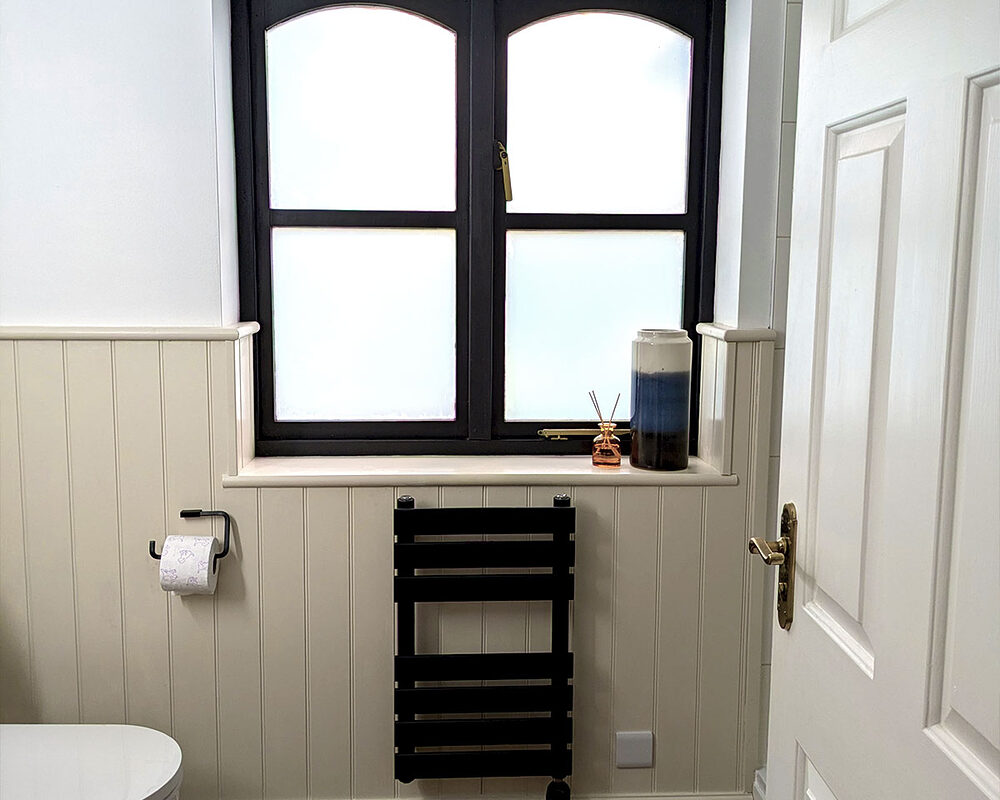 Casement dark window in bathroom with cream-coloured wooden wall panelling - all installed by River ODP in Jevington