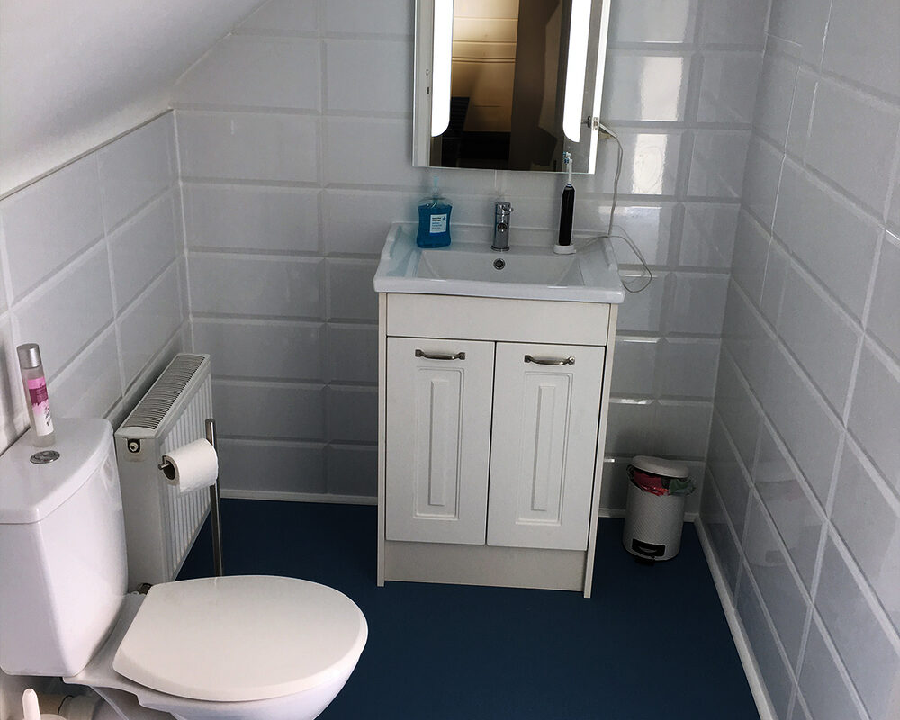 Loft bathroom with angled wall storage and glass shower in Seaford by River.ODP bathroom specialists.