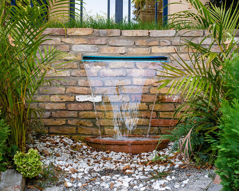 Wide water blade mounted in brick wall in garden in Kent